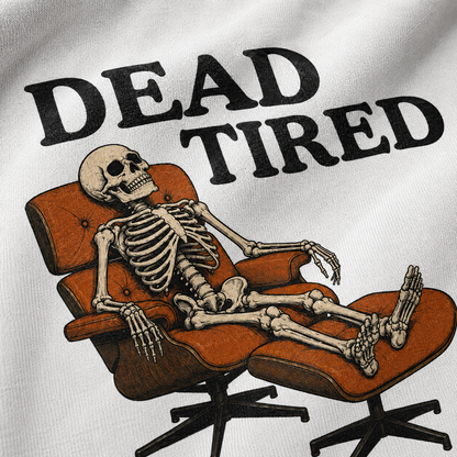 A close-up of a white fabric surface printed with the phrase 'DEAD TIRED' in large black letters above an illustrated skeleton reclining in an orange lounge chair with an ottoman.