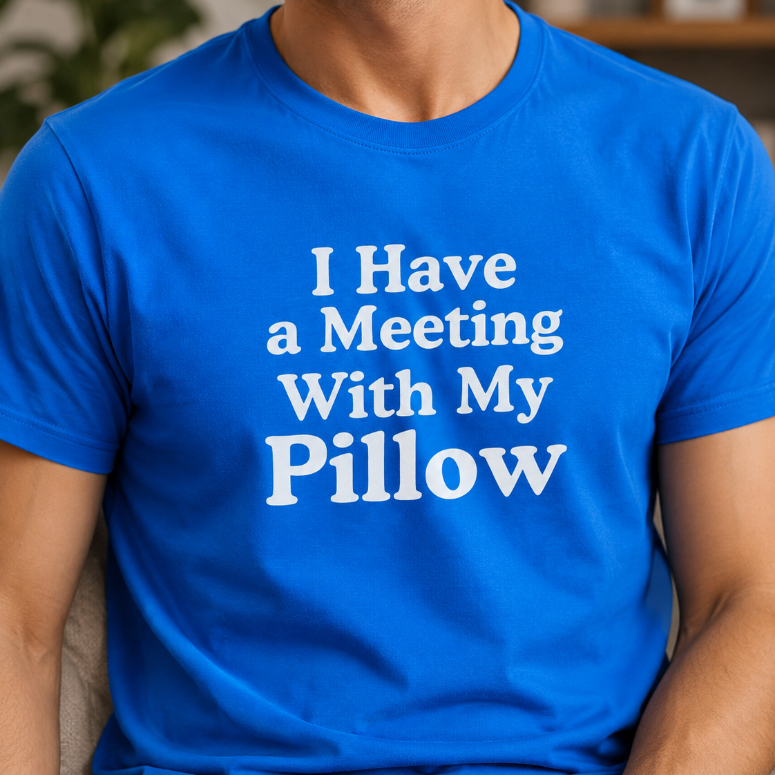 A man wearing a bright blue crewneck t-shirt with the text 'I Have a Meeting With My Pillow' printed in white on the chest, set against a blurred indoor background.