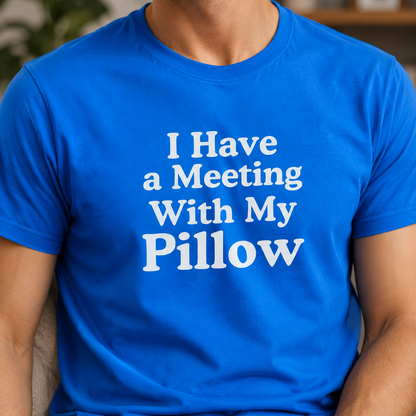 A man wearing a bright blue crewneck t-shirt with the text 'I Have a Meeting With My Pillow' printed in white on the chest, set against a blurred indoor background.