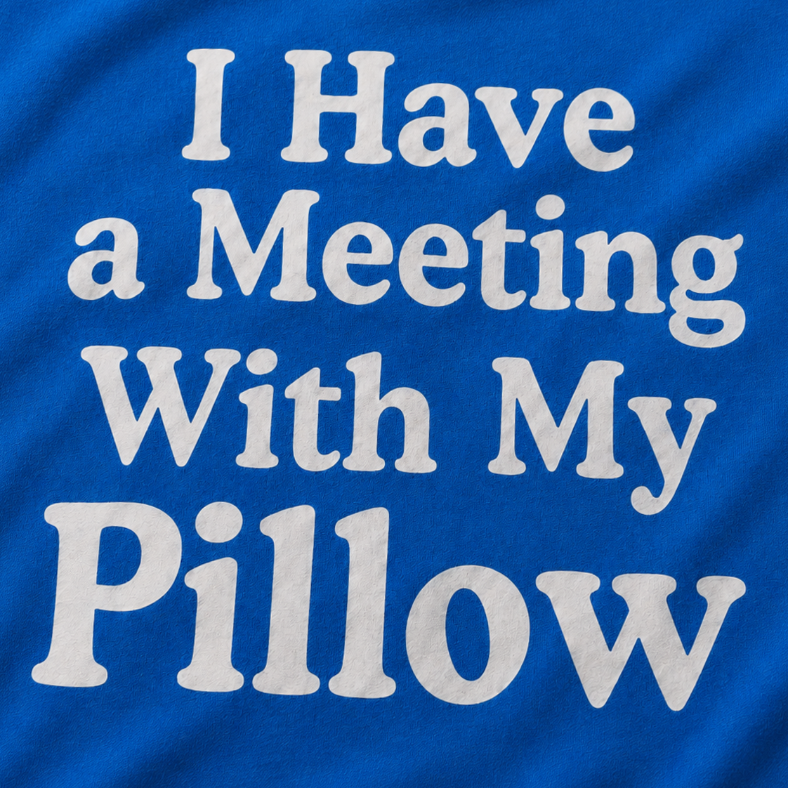 A close-up of a royal blue t-shirt featuring the phrase 'I Have a Meeting With My Pillow' printed in a large, white, stylized font across the front.