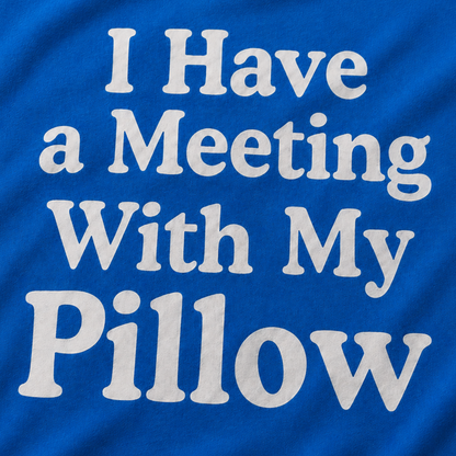 A close-up of a royal blue t-shirt featuring the phrase 'I Have a Meeting With My Pillow' printed in a large, white, stylized font across the front.