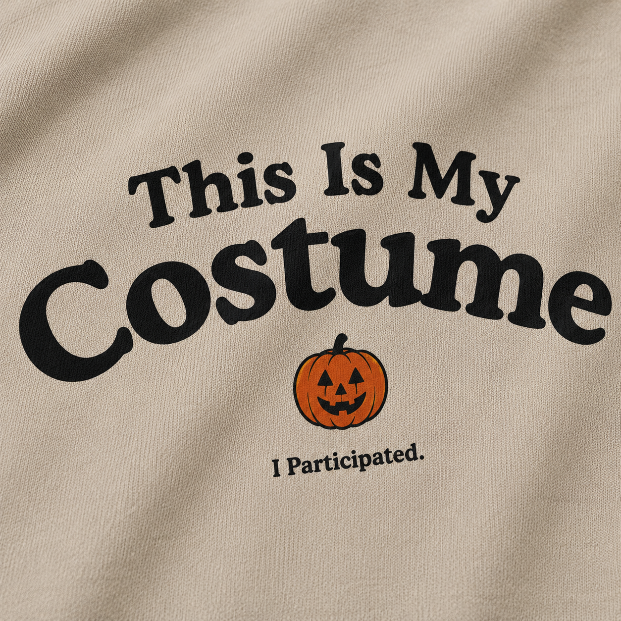 Close-up of a beige fabric garment with black text reading 'This Is My Costume' and a small orange jack-o'-lantern graphic, plus 'I Participated.' underneath.