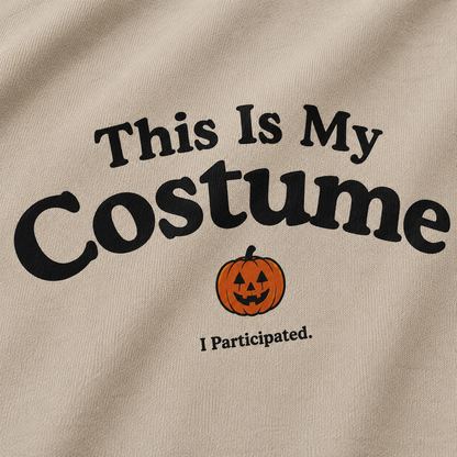 Close-up of a beige fabric garment with black text reading 'This Is My Costume' and a small orange jack-o'-lantern graphic, plus 'I Participated.' underneath.